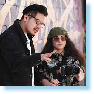 young woman and young man in front of wall with mural