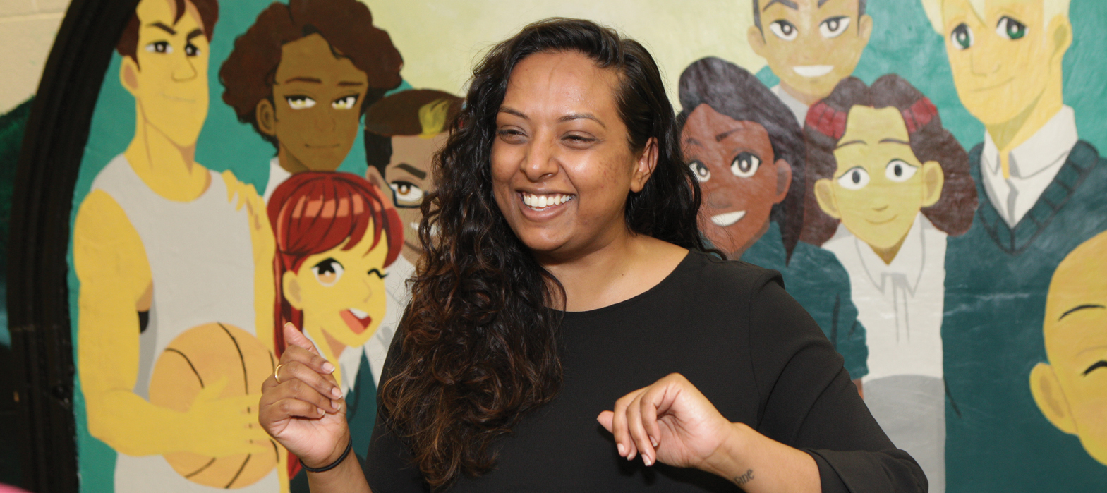 smiling teacher in front of multicultural mural