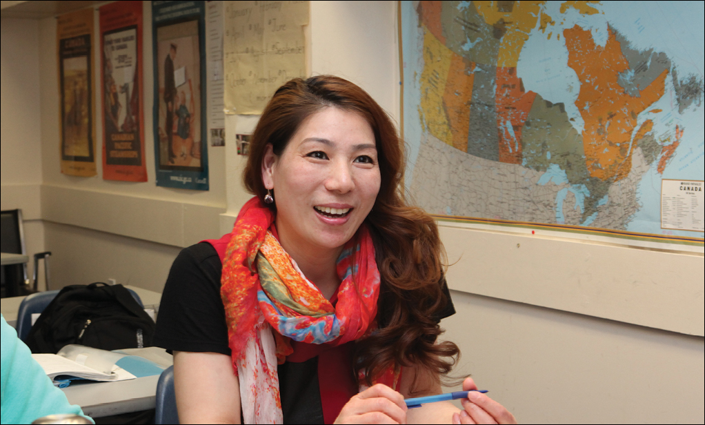 newcomer woman sitting in classroom with map of Canada in the background